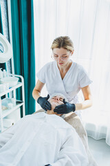 A smiling cosmetologist is doing a beauty procedure on her patient. Facial skin care. Cosmetology and dermatology.