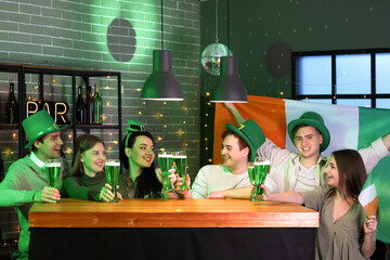 Group of young people with beer and Irish flag celebrating St. Patrick's Day at counter in pub