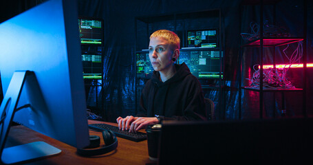 Caucasian woman with short blond hair working in cyber security center and analyzing data. Female hacker typing on keyboard at big computer in dark monitoring room.