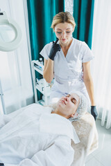 A smiling cosmetologist is doing a beauty procedure on her patient. Facial skin care. Cosmetology and dermatology.