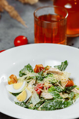 Traditional caesar salad in a white bowl on a old white table with leaves and a sauce boat and parmesan. Selected focus.