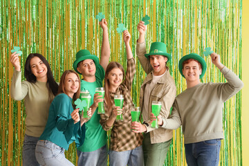 Group of young people with beer against tinsel on yellow background. St. Patrick's Day celebration