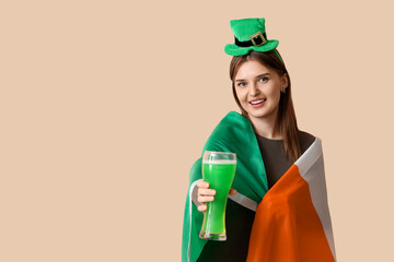 Young woman with beer and Irish flag on beige background. St. Patrick's Day celebration
