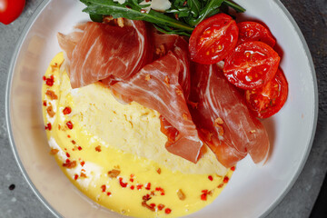 Crepes with fried egg, Jamon slices, fresh tomatoes and cucumber fillings on a white plate on an old wooden table, view from above