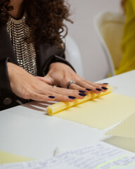 Elegant woman rolling a beeswax sheet to make a candle, with notes and craft tools on a white surface