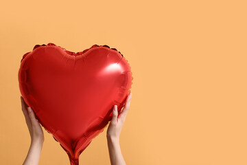 Female hands with heart shaped air balloon on yellow background. Valentine's Day celebration