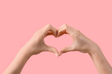 Obraz premium Female hands showing heart gesture on pink background. Valentine's Day celebration