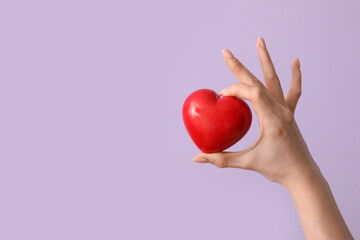 Female hand with heart on lilac background. Valentine's Day celebration