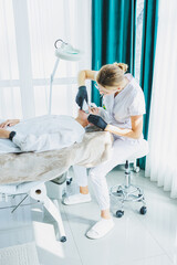 A dermatologist or cosmetologist in a clinic works with female patients and makes facial skin procedures on a young woman's face. Ultrasonic cleaning of the face in the cosmetologist's office