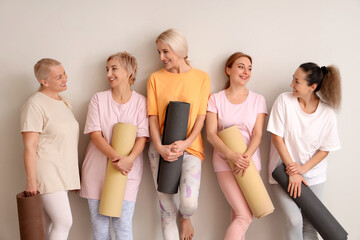 Group of mature women with yoga mats on light background