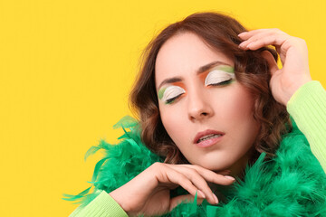 Woman with festive Irish makeup and feather boa on yellow background. St. Patrick's Day celebration