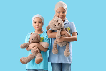 Cute little children after chemotherapy with yellow ribbons and teddy bears on blue background....