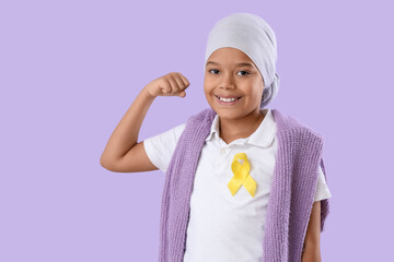 Cute little African-American boy after chemotherapy with yellow ribbon showing muscles on lilac...