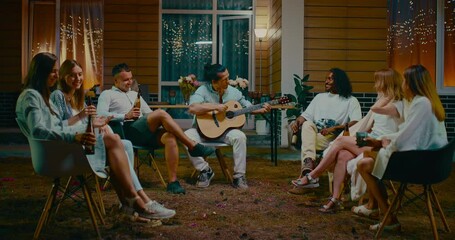 Hispanic man playing guitar for friends in merry backyard party, people singing songs, 4K, Prores