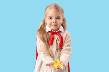 Cute little girl in superhero costume with yellow ribbon on blue background. Childhood cancer awareness concept