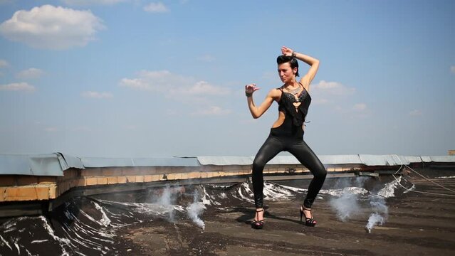 Cute girl dances on roof with smoke at background of blue sky
