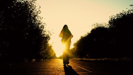 Rear view of man walking on road at sunset. Woman with backpack walks along an asphalt road towards sun. Outdoor travel concept. Tourist goes on an adventure trip vacation, nature. Hiker with backpack