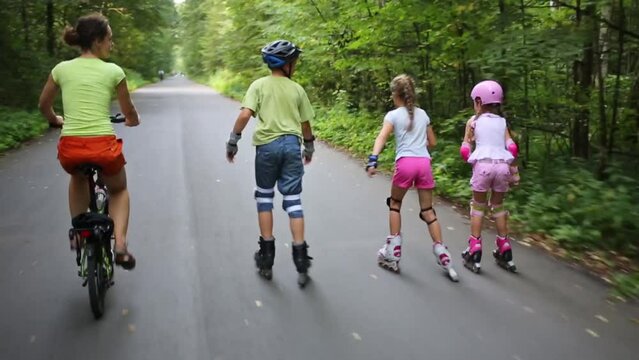 Back of children riding on roller skates and woman riding bicycle