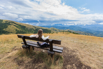 Naklejka na ściany i meble Child enjoying scenic mountain nature landscape view, sitting on the bench, feeling peaceful and connected with nature. 
