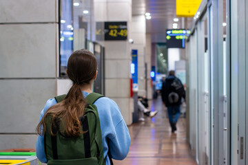 Beautiful young woman walking to airport lounge with a green backpack after security check. Travel...