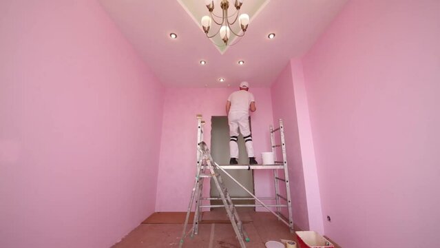 Man with brush in hand standing on scaffolding in pink room