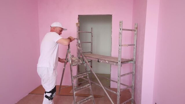 Man in white moves scaffolding in pink new room before work