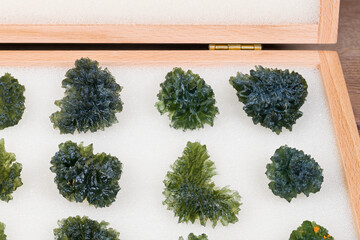 Closeup a collection of raw green moldavite gems in wooden storage locker. Group of uncut precious...