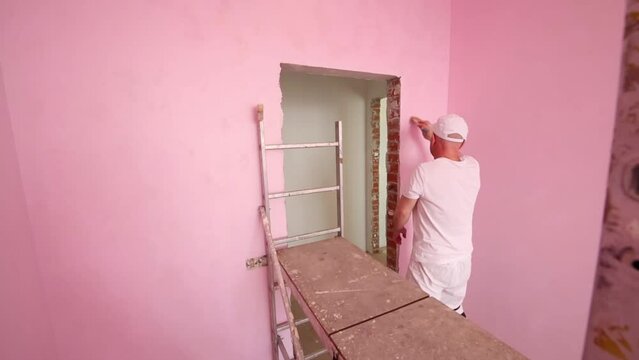 Worker in cap and white clothes paints wall in new pink room