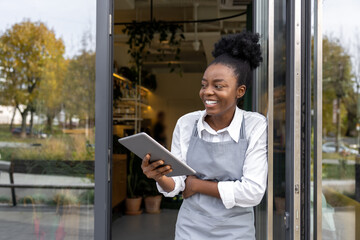 Dark-skinned young woman with notepad in hands standing in cafe door