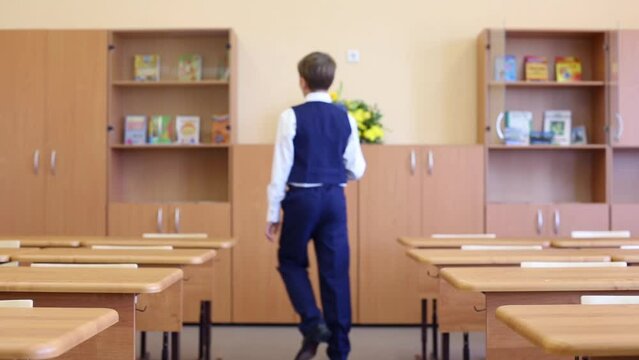 Back of boy in uniform going among desks in classroom