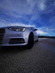 headlight of modern prestigious car on winter road under blue cloudy sky. Front lights with...