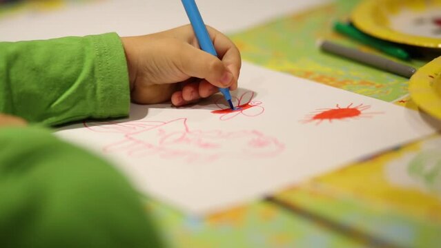 Hands of little girl drawing picture by colored markers on table