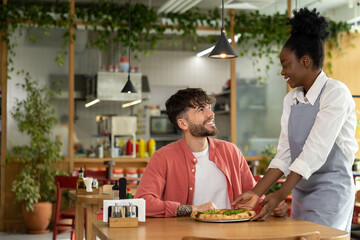 Fototapeta na wymiar Young dark-skinned waitress putting pizza on a customers table