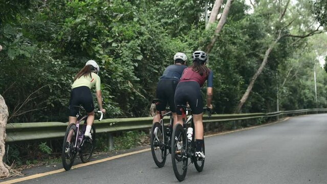 rear view of three asian young cyclists riding bike on slope of rural road