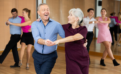 Cheerful elderly amateur couple visiting group choreography class, practicing vigorous lindy hop...