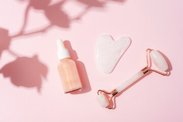 Obraz na płótnie Canvas Cosmetic serum bottle, face roller and gua sha stone with orchid flower shadow on pink background. Sharp shadows. Home spa concept. Top view, flat lay