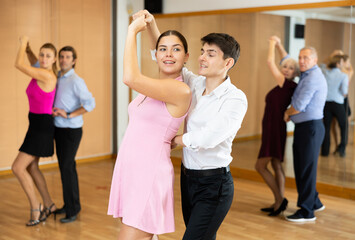 Cheerful young guy and girl practicing ballroom dances in ballroom - obrazy, fototapety, plakaty
