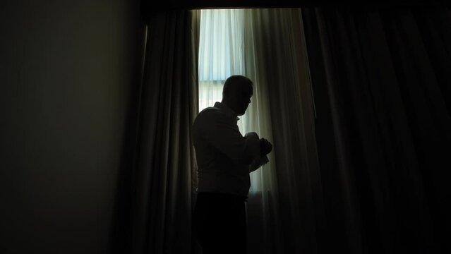 Close up view of silhouette A man putting on his cufflinks in room on the background of the window. 