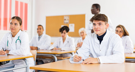 Group of young men and women in lab coats lesitening to professor during classes in medical college.