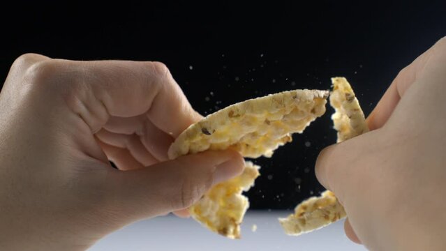 Macro close-up of hand breaking cracker with crumbs flying in the air in super slow motion