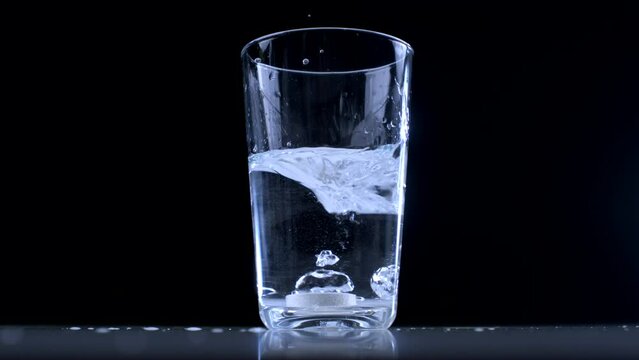 Dropping effervescent Vitamin C tablet into water on glass cup - black backdrop