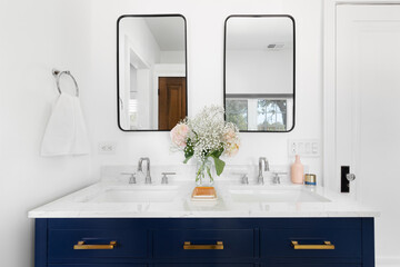 A bathroom detail with a blue cabinet and gold hardware, flowers on the white marble countertop,...