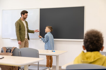 Teacher working with boy pupil at lesson solving math tasks in classroom in school.