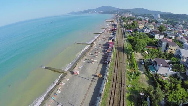 Many tourists get rest on sea beach near railway in coastal city
