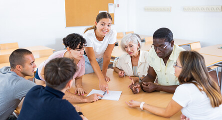 Adult students of different ages and teacher brainstorming round table in university classroom - obrazy, fototapety, plakaty