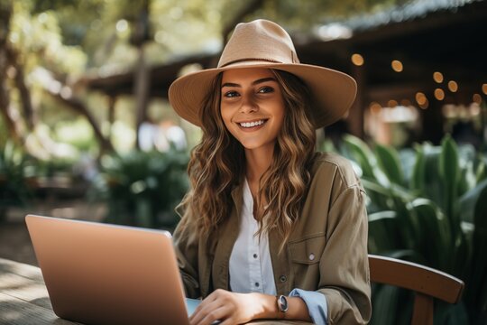 Smiling Young Woman Wearing A Hat And Using A Laptop Outdoors