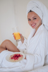 Cute young woman in bath robe having breakfast and feeling enjoyed