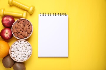 Notebook, fresh fruits and almonds on yellow background, flat lay. Low glycemic index diet