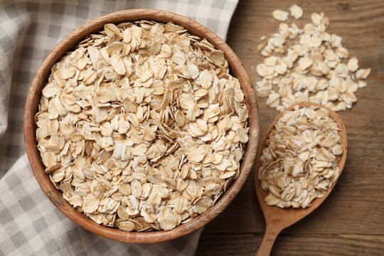 Bowl and spoon with oatmeal on wooden table, flat lay