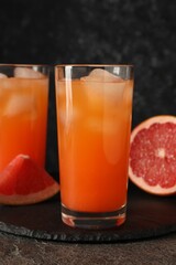 Tasty grapefruit drink with ice in glasses and fresh fruits on dark textured table